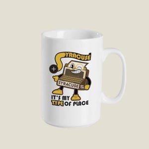 May include: White ceramic mug featuring a cartoon typewriter character with the text "YRACUSE" and "IT'S MY TYPE OF PLACE". The design includes yellow, brown, and black accents, with the words "Syracuse New York".