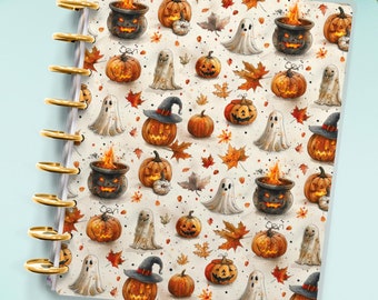 May include: A Halloween-themed planner with a white cover featuring a repeating pattern of pumpkins, ghosts, and cauldrons. The planner has a gold coil binding.