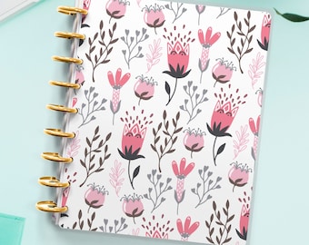 Op de afbeelding: Een witte planner met een bloemenpatroon met roze en grijze bloemen en bladeren. De planner heeft gouden ringen en een transparante hoes.