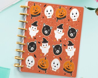 May include: A Halloween-themed planner with a orange and white cover featuring a repeating pattern of ghosts, pumpkins, cats, and skulls. The planner has gold rings and a clear plastic cover.