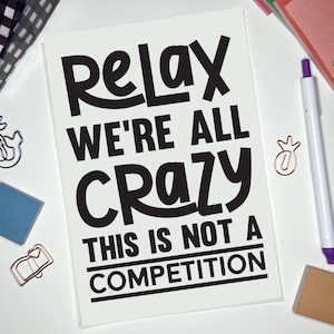 May include: White background with a black and white sign that reads "Relax We're All Crazy This Is Not A Competition".