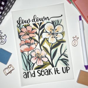 May include: A white background with a floral design and the text "slow down and soak it up".