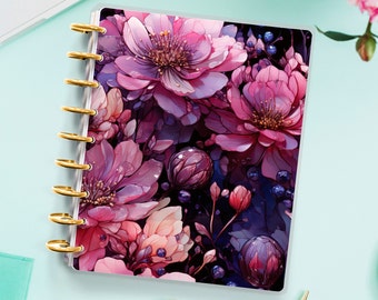 Op de afbeelding: Een bloemenplanner met een roze en paarse bloemenprint. De planner heeft een gouden spiraalbinding en een transparante omslag.