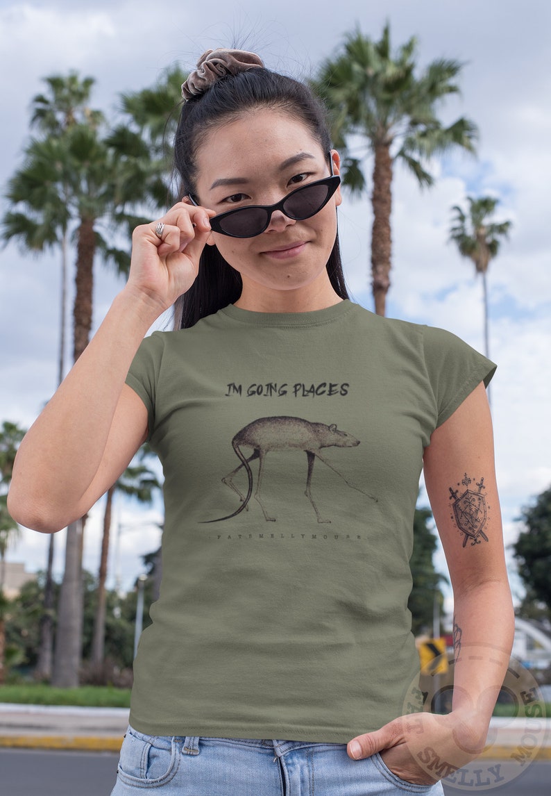May include: A green t-shirt with a graphic of a rat with the text "I'm going places" and the artist's name "Fatimelly Mouse" printed on the front.