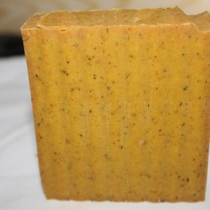 Peut inclure: Une barre de savon rectangulaire jaune avec des taches brunes partout. Le savon a une surface rugueuse et texturée.