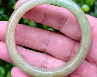 May include: A smooth, circular bangle bracelet crafted from translucent light green jade stone. The bangle features a polished, rounded surface with subtle variations in color, ranging from pale cream to soft mint green throughout the stone.