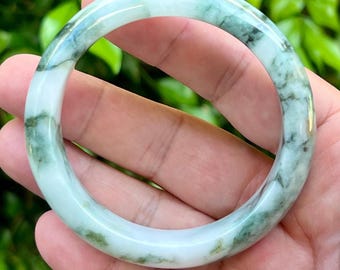 Op de afbeelding: Een gladde, ronde armband van gepolijste steen, met een doorschijnende witte basiskleur en opvallende, onregelmatige vlekken en aders in diep bosgroen over het gehele oppervlak van de afgeronde band.