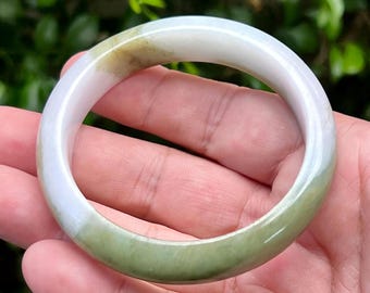 May include: A smooth, circular bangle bracelet crafted from polished stone. The piece features a translucent white base color with distinct patches of pale green and soft olive-toned inclusions throughout the rounded, solid band structure.