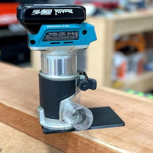 May include: A blue and black cordless Makita XTR01 router with a 18V LXT battery attached. The router is sitting on a wooden surface.