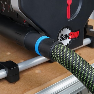 May include: Close-up of a black and green dust collection hose connected to a black dust port on a SawStop table saw. The hose has a blue ring around the connection point.