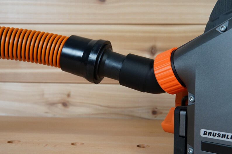 May include: Close-up of a black and orange power tool with a dust collection hose attached. The tool has a black body with an orange dust port and a black hose with an orange corrugated section. The tool has the word "BRUSHLESS" printed on it.