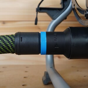 May include: A black vacuum hose with a green and black patterned sleeve and a blue ring. The hose is connected to a black vacuum cleaner.