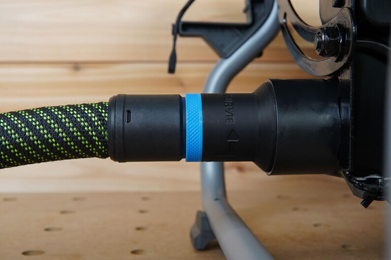 May include: A black vacuum hose with a green and black patterned sleeve and a blue ring. The hose is connected to a black vacuum cleaner.