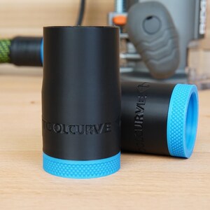 May include: Two black cylindrical objects with blue textured bases. The text "TOOLCURVE" is embossed on the side of each object. One object is upright, and the other is lying on its side. A power tool is in the background.