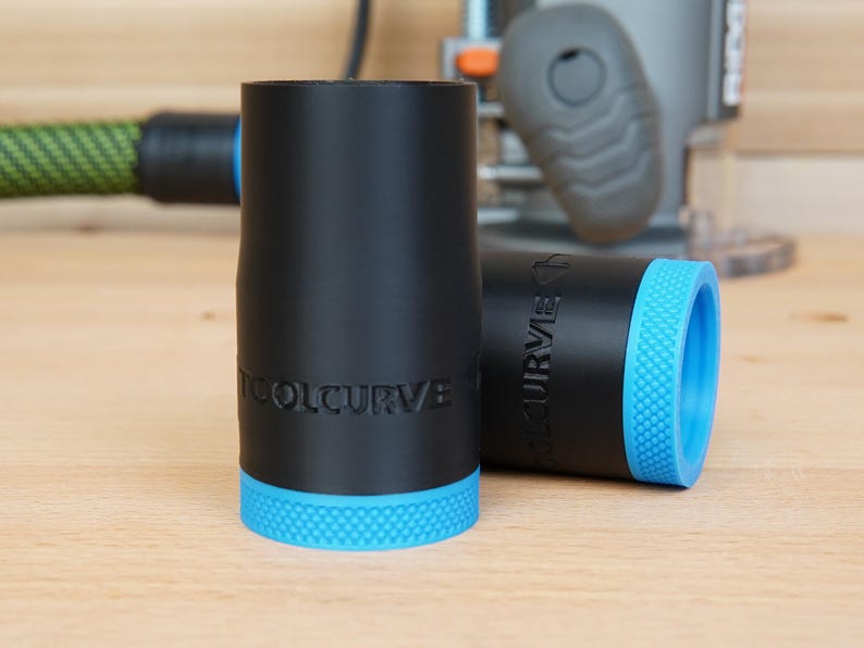 May include: Two black cylindrical objects with blue textured bases. The text "TOOLCURVE" is embossed on the side of each object. One object is upright, and the other is lying on its side. A power tool is in the background.