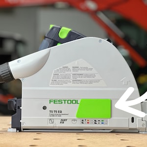 Op de afbeelding: Een witte en groene Festool TS 75 EQ-zaag met een zwart en grijs handvat. De zaag heeft een groen label met de tekst "Festool TS 75 EQ" en "Product & Service Questions? Call 1-800-237-4440".