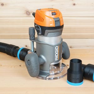May include: A grey and orange RIDGID router with a black hose and two black attachments with blue accents. The router is on a light brown wooden surface.