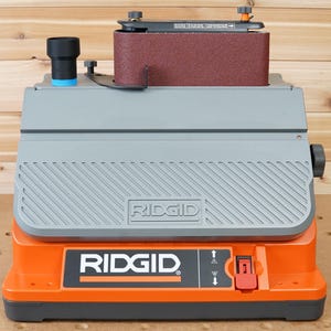May include: An orange and grey Ridgid belt sander with a red power switch. The sander has a dust collection port and a belt sander attachment.