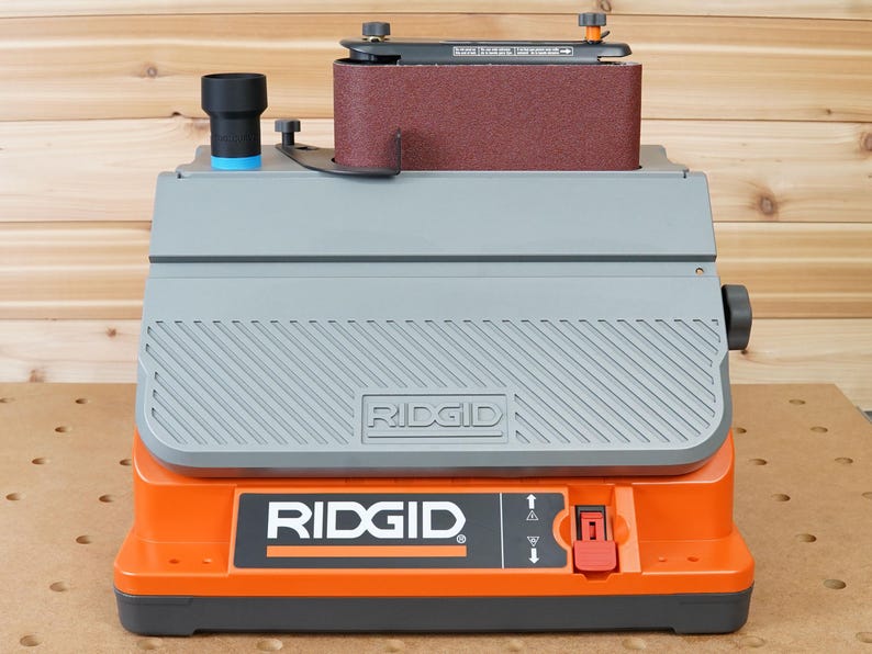 May include: An orange and grey Ridgid belt sander with a red power switch. The sander has a dust collection port and a belt sander attachment.