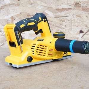 May include: A yellow and black cordless electric planer with a black and blue dust collection hose. The planer has a black handle and a yellow base. The hose is connected to the planer with a black and blue connector.