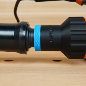 K&ouml;nnte beinhalten: Nahaufnahme eines orange-schwarzen Elektroschleifers mit angeschlossenem Schlauch. Der Schlauch ist orange und gewellt und verbindet sich mit einem schwarzen Adapter mit blauem Ring. Der Schleifer ist orange und schwarz.