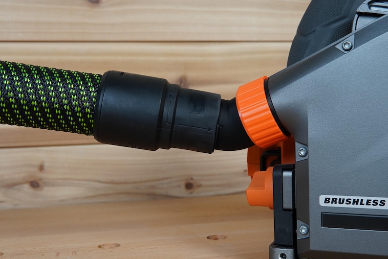 May include: A close-up of a black and orange power tool with a dust collection hose attached. The tool has a "BRUSHLESS" label on the side.