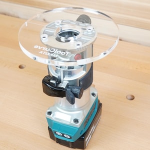 May include: A cordless power router with a clear plastic base and a silver and teal body. The router has a black handle and a battery pack attached to the bottom. The brand name "ToolCraze" is printed on the clear base.