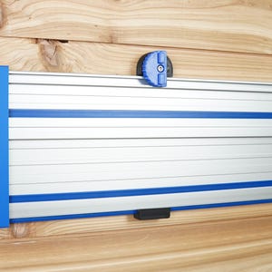 Puede incluir: Un sistema de rieles de pared plateado y azul con una perilla azul. El riel está hecho de metal y tiene una franja azul que recorre la parte superior e inferior.