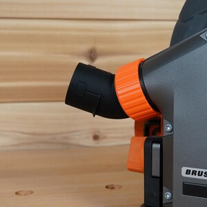 May include: Close-up of a gray power tool with an orange dust port and a black dust collection hose. The tool has a "BRUSHLESS" label on the side.