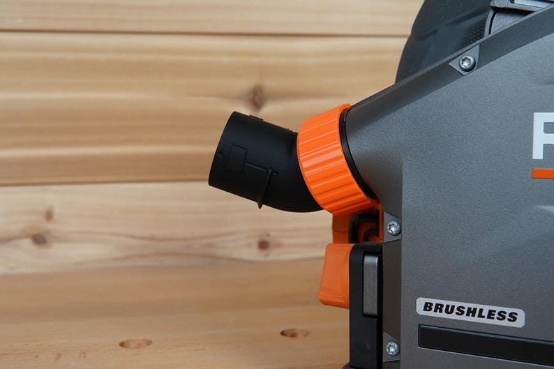 May include: Close-up of a gray power tool with an orange dust port and a black dust collection hose. The tool has a "BRUSHLESS" label on the side.