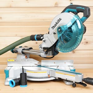 May include: A Makita mitre saw in teal and grey. The saw has a clear blade guard, a black handle, and a green and black hose. It is designed for cutting wood and other materials, and is suitable for DIY projects.