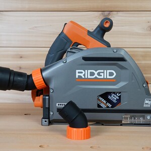 May include: A gray and orange RIDGID circular saw with a dust collection port and a 70 carbide tooth blade. The saw is on a wooden surface.