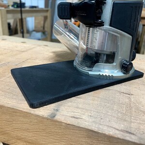 May include: A black base plate for a router, with a silver and black router on top. The router has a clear plastic cover and a depth gauge marked in millimeters.