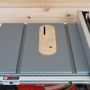 Może przedstawiać: Szara piła stołowa z drewnianym wkładką na ostrze. Piła stołowa ma prowadnicę i kątownik.