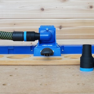 Könnte beinhalten: Eine blaue und schwarze Holzbearbeitungslehre mit einem Staubabsauganschluss und zwei schwarzen Staubabsaugadaptern. Die Lehre hat eine Reihe von Löchern zum Bohren von Taschenlöchern.