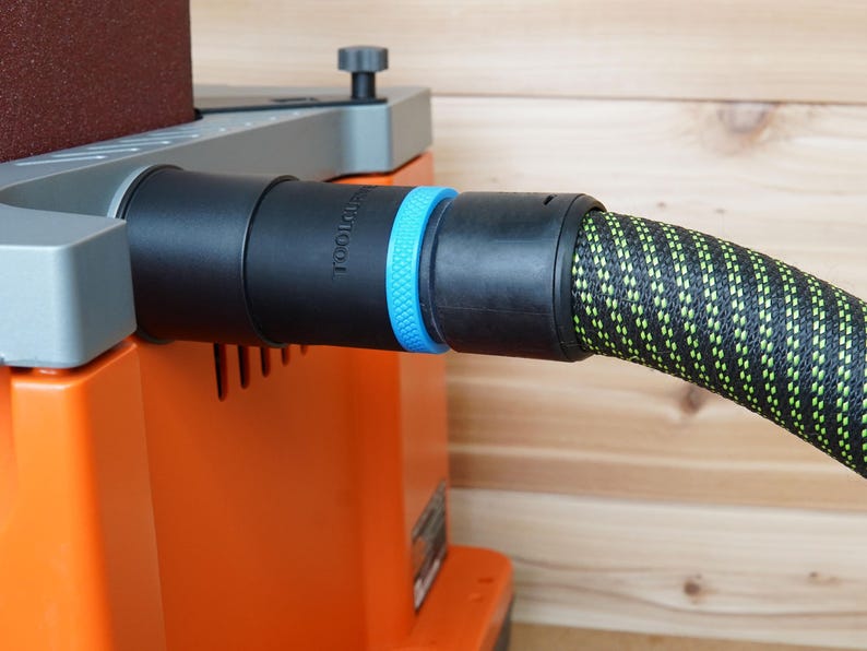 May include: A black and green dust collection hose connected to a sander with a blue and black dust port. The sander has a gray top and an orange base. The text "TOOLCRAFT" is printed on the sander.