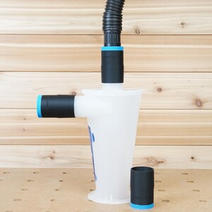 Könnte beinhalten: Ein weißes Kunststoff-Staubsammelsystem mit einem schwarzen Schlauch und blauen Verzierungen. Das System verfügt über einen großen, zylindrischen Behälter mit einem kleineren, zylindrischen Behälter, der an der Seite befestigt ist. Das System ist für die Staubaufnahme von Holzbearbeitungswerkzeugen konzipiert.