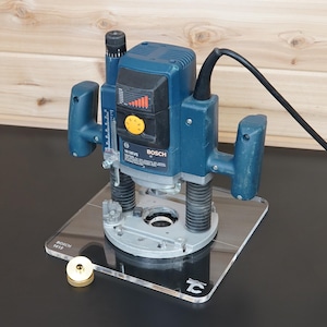 Peut inclure: Une défonceuse plongeante Bosch 1613EVS bleue avec deux poignées ergonomiques, un cordon d'alimentation noir et une plaque de base carrée transparente. L'outil comprend une molette de vitesse jaune, une échelle de profondeur et un guide circulaire en laiton.