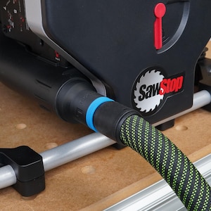 Puede incluir: Primer plano de una sierra de mesa SawStop negra con una manguera de aspiración de polvo verde y negra conectada a la sierra. La manguera tiene un conector azul y negro.