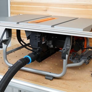 May include: A gray table saw with a black motor and a black dust collection hose. The saw is on a wooden stand with a gray metal frame.