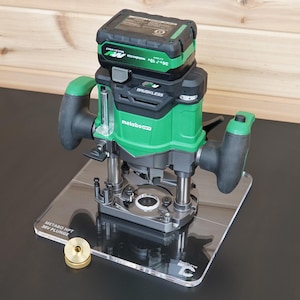 May include: A green and black Metabo HPT 36V cordless plunge router mounted on a clear acrylic base plate. The tool features a brushless motor, two ergonomic handles, and a battery pack. A small brass circular guide bushing sits on the base.