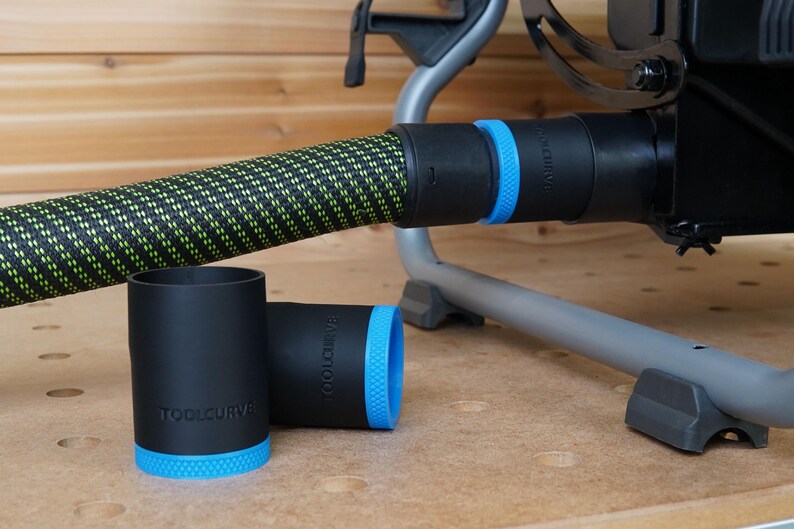 Puede incluir: Dos adaptadores de colector de polvo negros con ribete azul y el texto "TOOLCURVE" impreso en ellos. Los adaptadores est&aacute;n conectados a una manguera de polvo negra y verde.