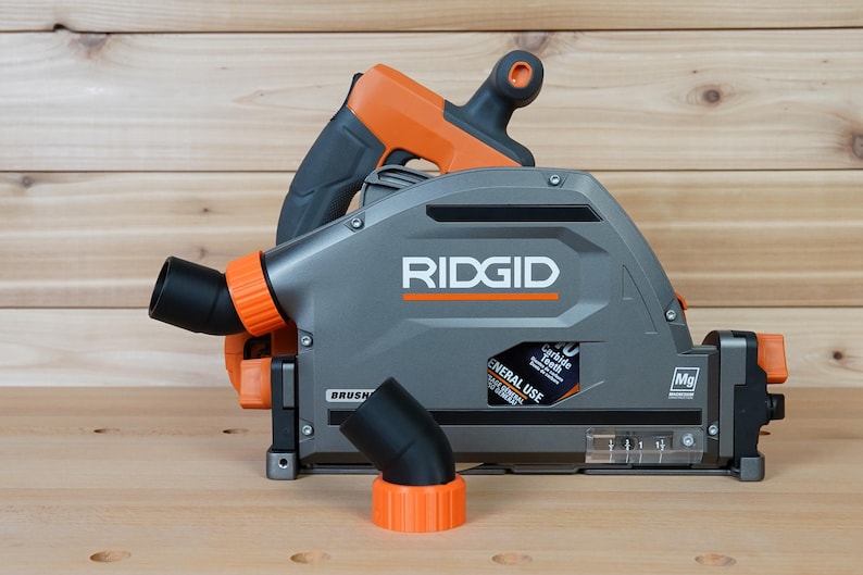 May include: A gray and orange RIDGID circular saw with a dust port and a 7-1/4 inch blade. The saw has a black dust collection hose attached to the dust port. The saw is sitting on a wooden surface.