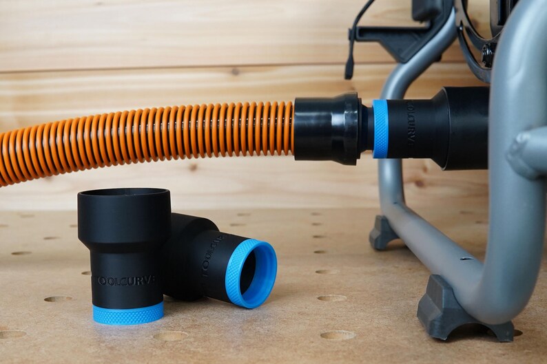 Op de afbeelding: Een close-up van een zwarte en oranje stofzuigerslang met een zwarte stofzuigeradapter. Twee zwarte stofzuigeradapters met blauwe ringen liggen op een houten oppervlak.