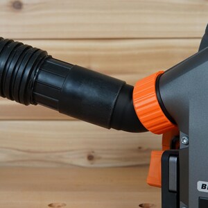 May include: Close-up of a black and orange power tool with a dust collection hose. The tool has a "BRUSHLESS" label on the side.