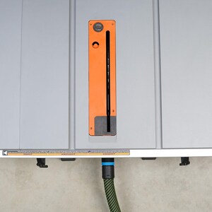 May include: A grey table saw with an orange and black blade guard. The saw has a dust collection port on the side and a power cord plugged in. The saw is sitting on a concrete floor.