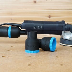 May include: A black and blue power sander with a dust collection hose and two black and blue dust collection adapters. The sander has a green lever and a silver base.