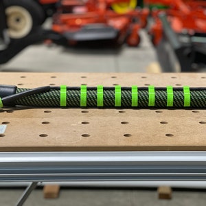 May include: A black and green hose with a black connector on one end and green bands around the hose. The hose is lying on a wooden surface with holes.
