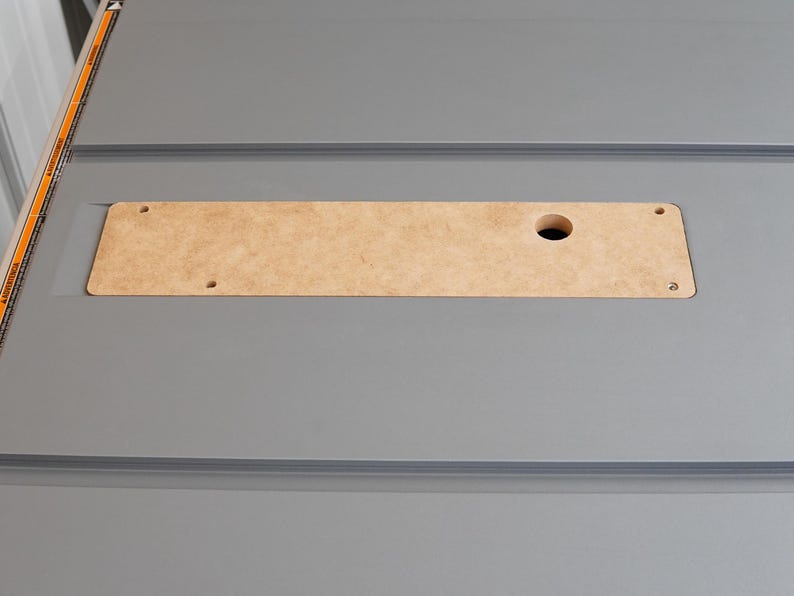 Puede incluir: Primer plano de una mesa de color gris con una inserci&oacute;n rectangular de madera. La inserci&oacute;n tiene un agujero redondo en el centro y dos peque&ntilde;os agujeros a cada lado.