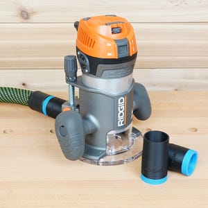 May include: A grey and orange RIDGID router with a clear base, a green and black hose, and two black and blue accessories. The router is on a light wood surface.